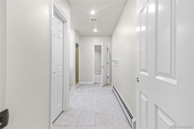 hallway with light tile patterned floors, a textured wall, visible vents, baseboards, and baseboard heating