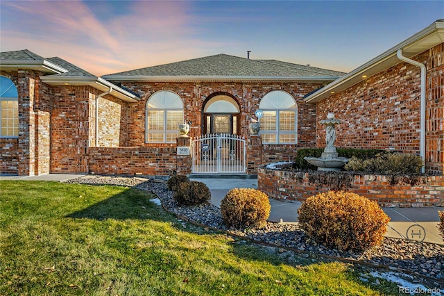 exterior space featuring a yard, brick siding, and a shingled roof