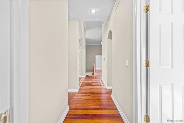 hall with baseboards, arched walkways, wood finished floors, and ornamental molding