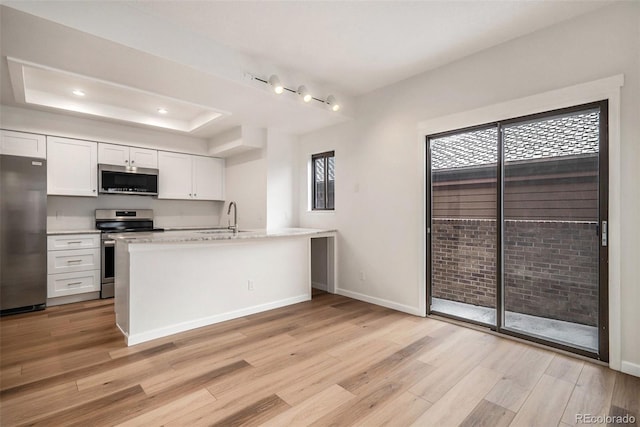 kitchen with appliances with stainless steel finishes, a tray ceiling, light wood-type flooring, and white cabinets