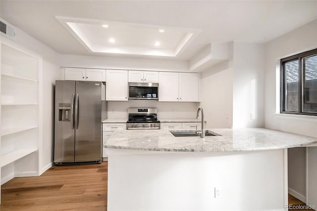 kitchen with appliances with stainless steel finishes, sink, white cabinets, light hardwood / wood-style floors, and light stone countertops