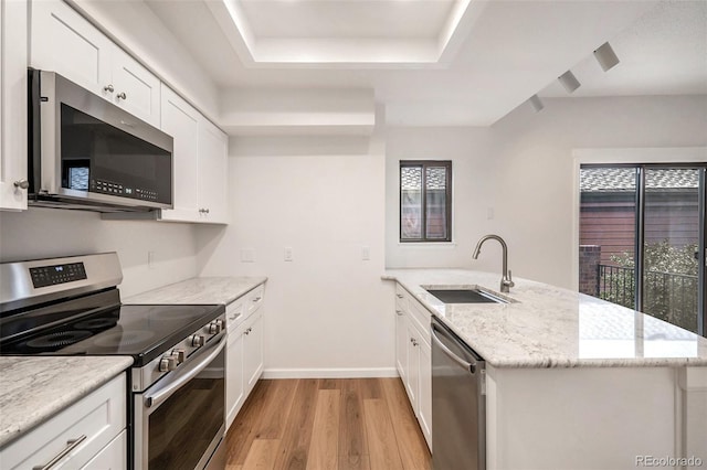 kitchen featuring sink, white cabinetry, light wood-type flooring, appliances with stainless steel finishes, and light stone countertops