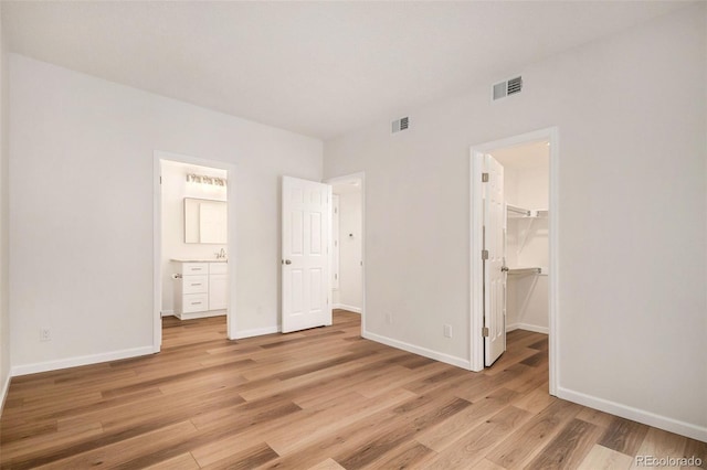 unfurnished bedroom with a walk in closet, ensuite bath, a closet, and light hardwood / wood-style flooring