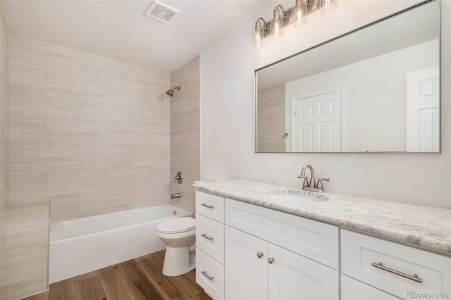 full bathroom with vanity, hardwood / wood-style floors, tiled shower / bath, and toilet