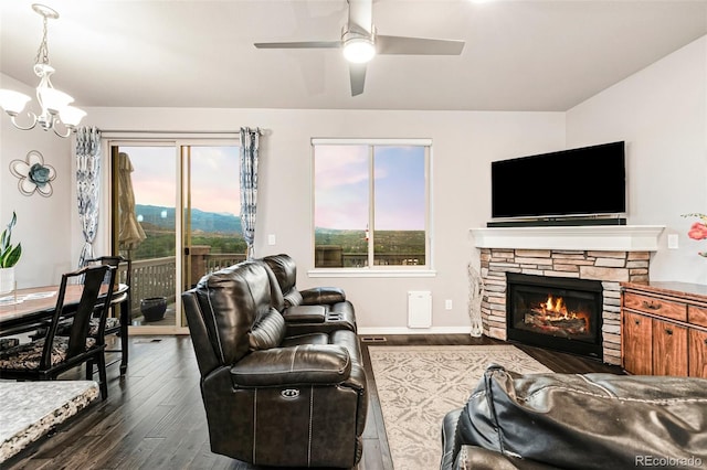 living room featuring ceiling fan with notable chandelier, dark wood-type flooring, and a fireplace