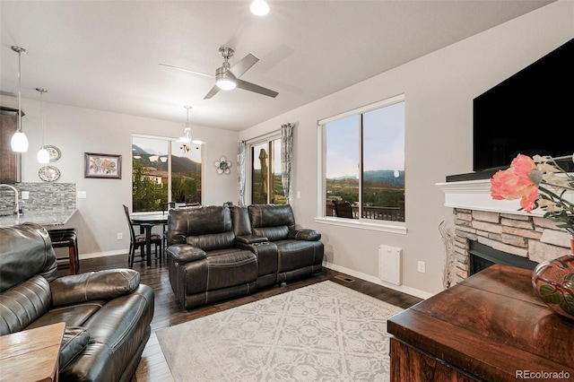 living room with a stone fireplace, hardwood / wood-style flooring, and ceiling fan