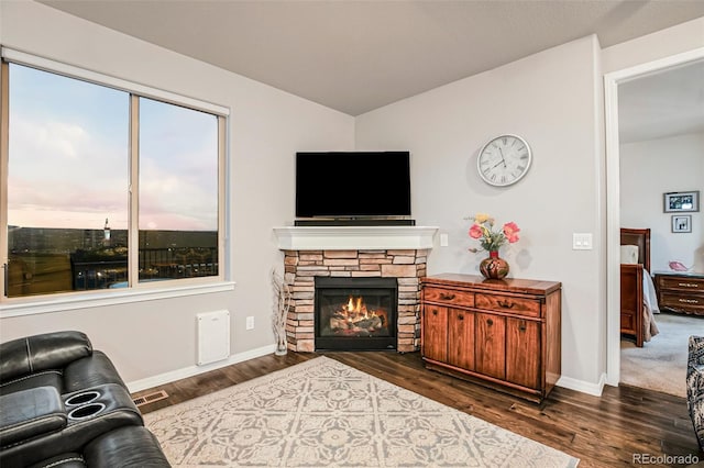 living room with dark wood-type flooring and a stone fireplace