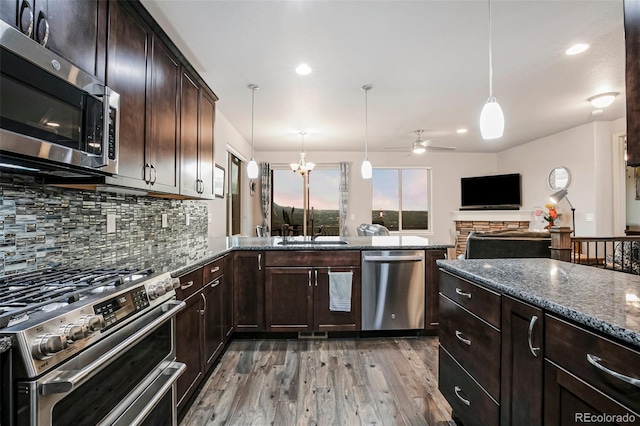 kitchen featuring wood-type flooring, dark stone countertops, stainless steel appliances, dark brown cabinetry, and decorative light fixtures