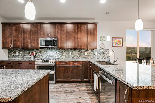 kitchen with light stone countertops, appliances with stainless steel finishes, sink, hanging light fixtures, and light hardwood / wood-style floors