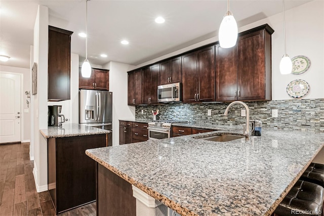 kitchen featuring dark wood-type flooring, kitchen peninsula, sink, light stone countertops, and appliances with stainless steel finishes