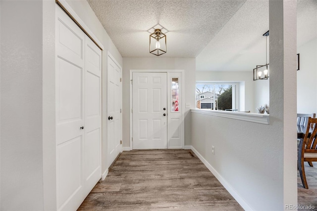 entrance foyer with baseboards, a textured ceiling, a notable chandelier, and wood finished floors