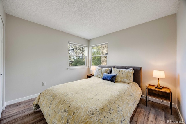 bedroom with a textured ceiling, baseboards, and wood finished floors