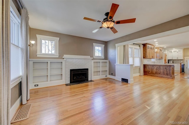 unfurnished living room featuring a brick fireplace, a wealth of natural light, and light hardwood / wood-style floors