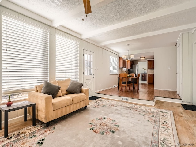 living room with beamed ceiling, a textured ceiling, ceiling fan with notable chandelier, and light hardwood / wood-style floors