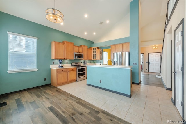 kitchen featuring a kitchen island, pendant lighting, high vaulted ceiling, stainless steel appliances, and light wood-type flooring