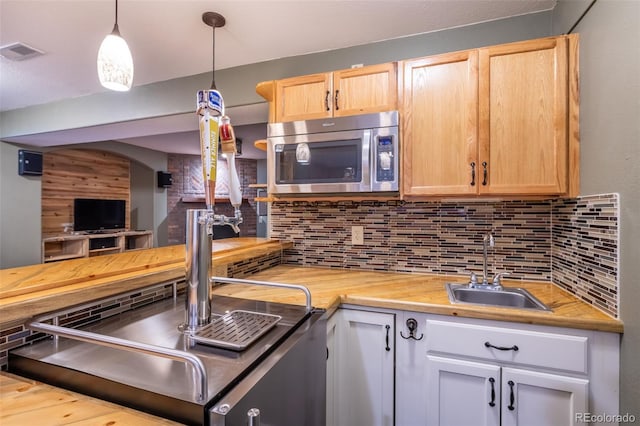 kitchen with wood counters, light brown cabinetry, sink, pendant lighting, and backsplash