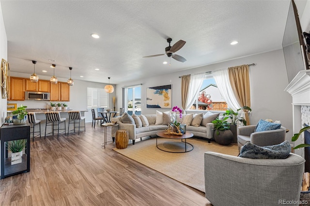 living room with ceiling fan, a textured ceiling, plenty of natural light, and light hardwood / wood-style floors