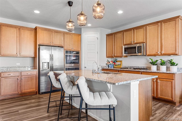 kitchen with hanging light fixtures, sink, a center island with sink, appliances with stainless steel finishes, and dark hardwood / wood-style flooring