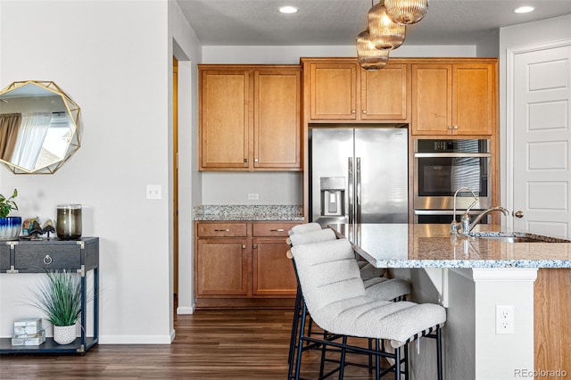 kitchen with a kitchen island with sink, sink, light stone counters, dark hardwood / wood-style floors, and appliances with stainless steel finishes