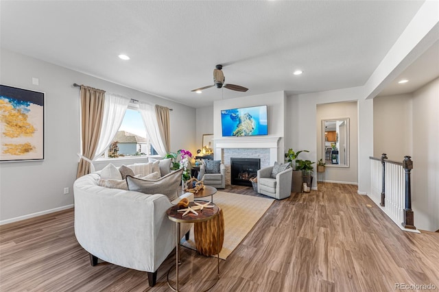 living room featuring ceiling fan, light hardwood / wood-style floors, a textured ceiling, and a stone fireplace