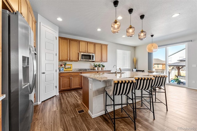 kitchen featuring dark hardwood / wood-style flooring, a kitchen breakfast bar, a center island with sink, decorative light fixtures, and stainless steel appliances