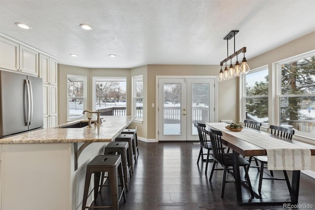 kitchen featuring light stone countertops, french doors, sink, a center island with sink, and hanging light fixtures