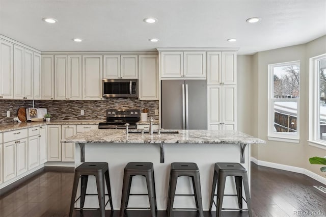 kitchen with appliances with stainless steel finishes, a center island with sink, light stone counters, and a breakfast bar area