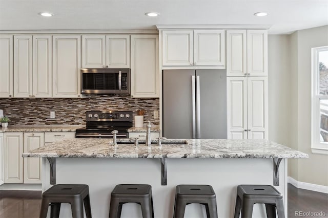 kitchen featuring sink, stainless steel appliances, light stone counters, an island with sink, and a breakfast bar area