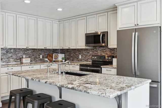 kitchen with a kitchen bar, light stone counters, white cabinets, and stainless steel appliances