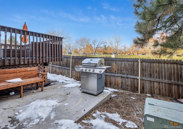 snow covered patio with a grill and a deck