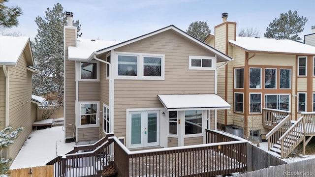 snow covered rear of property with a wooden deck and french doors