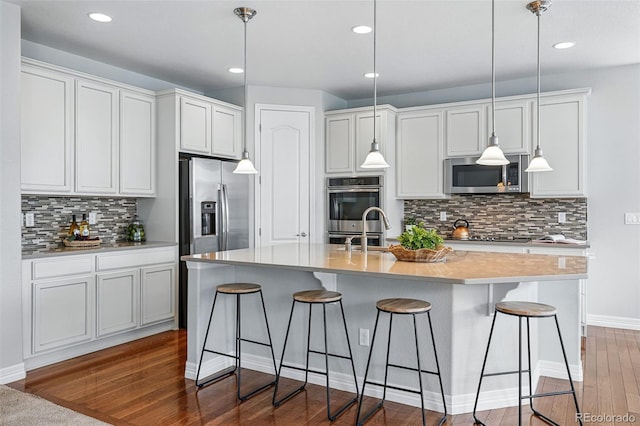 6013 Eldora St, Golden, CO 80403 - kitchen with appliances with stainless steel finishes, backsplash, a kitchen bar, decorative light fixtures, and dark wood-type flooring