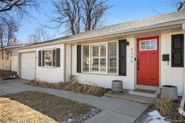 doorway to property with driveway, roof with shingles, an attached garage, and board and batten siding