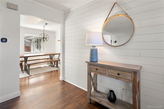 hallway with dark wood-style floors, a chandelier, crown molding, and baseboards