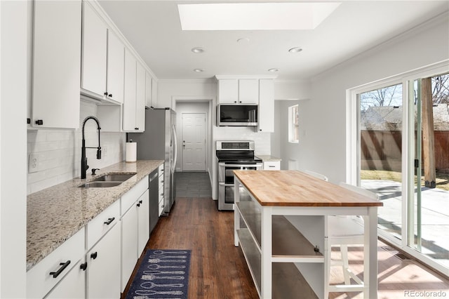 kitchen with a skylight, crown molding, appliances with stainless steel finishes, a sink, and butcher block countertops