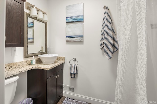 full bath featuring toilet, vanity, visible vents, and baseboards