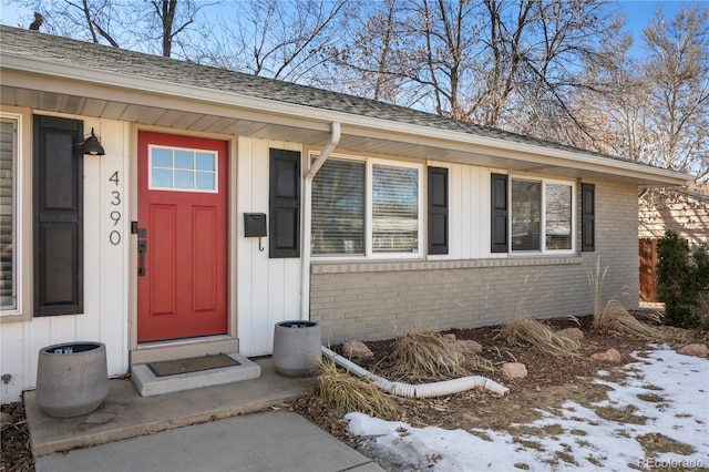 entrance to property with roof with shingles, board and batten siding, and brick siding