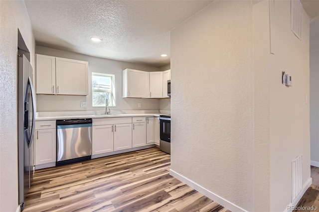 kitchen featuring stainless steel appliances, light hardwood / wood-style floors, sink, and white cabinets