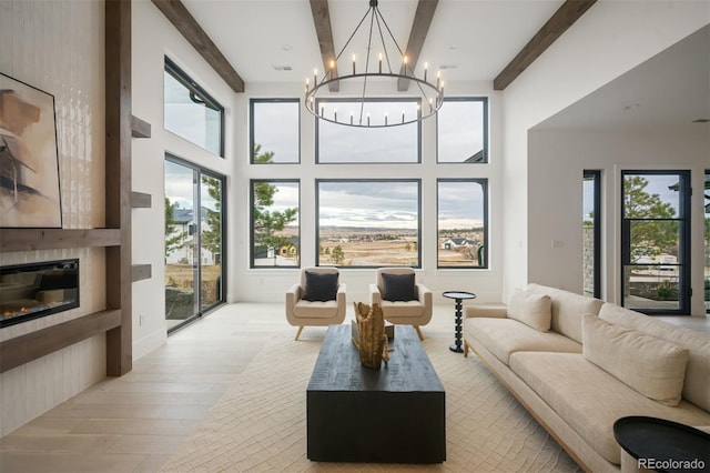 living room with a notable chandelier, beam ceiling, a fireplace, and light hardwood / wood-style floors