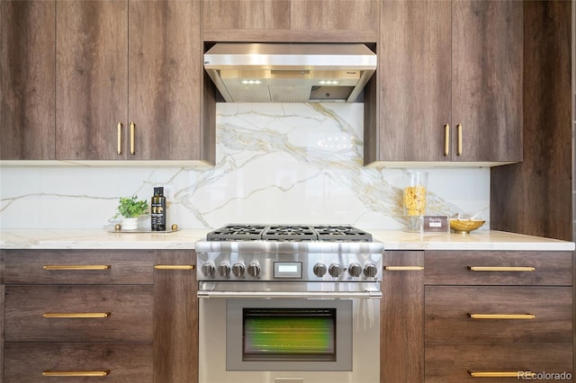 kitchen with high end range, wall chimney range hood, decorative backsplash, and light stone countertops