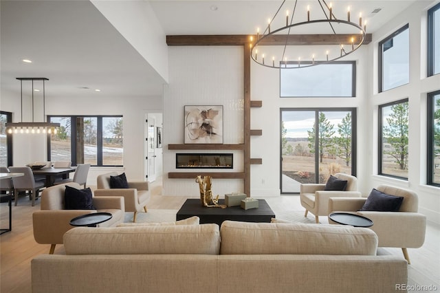 living room with beam ceiling, a large fireplace, an inviting chandelier, and light hardwood / wood-style flooring