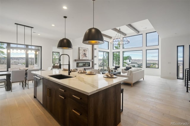 kitchen with sink, light stone counters, hanging light fixtures, an island with sink, and light hardwood / wood-style floors