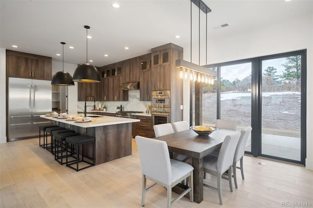 kitchen with stainless steel appliances, decorative light fixtures, extractor fan, and an island with sink