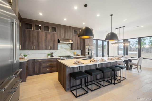 kitchen with stainless steel appliances, an island with sink, dark brown cabinets, and extractor fan