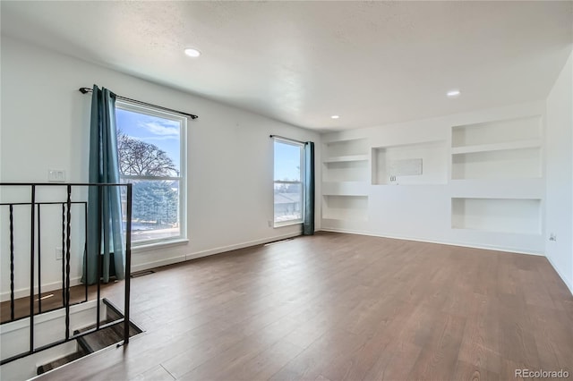 empty room with a textured ceiling, recessed lighting, wood finished floors, built in features, and baseboards