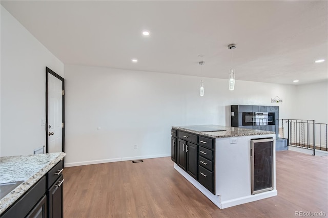 kitchen featuring wine cooler, dark cabinets, wood finished floors, hanging light fixtures, and a center island