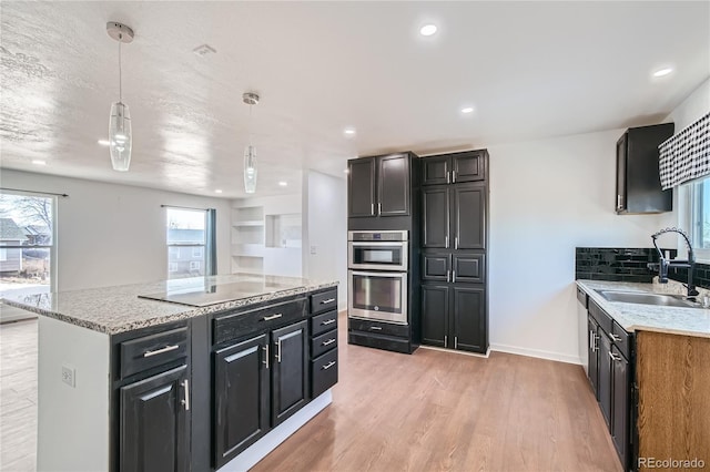 kitchen with light wood-style floors, pendant lighting, a sink, and light stone countertops