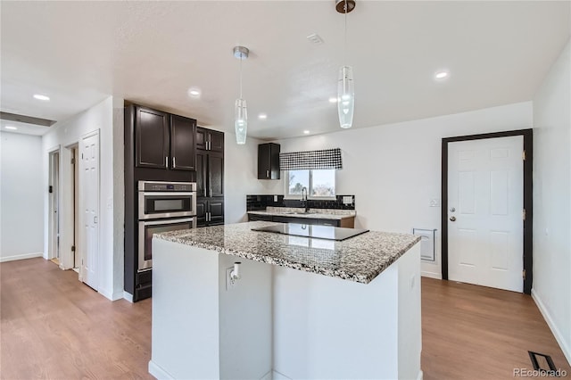 kitchen with black electric stovetop, a kitchen island, decorative light fixtures, and light stone countertops