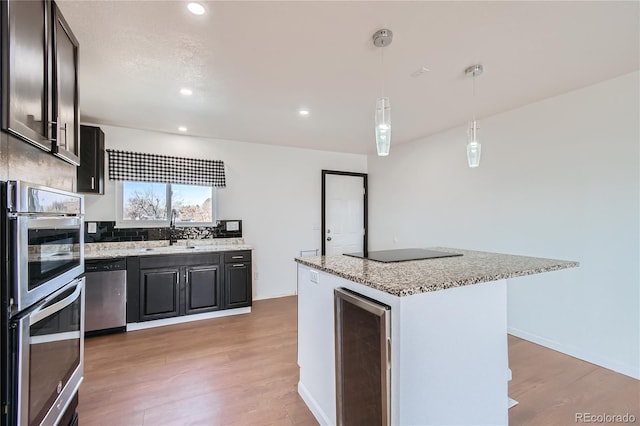 kitchen featuring a center island, stainless steel appliances, hanging light fixtures, a sink, and beverage cooler