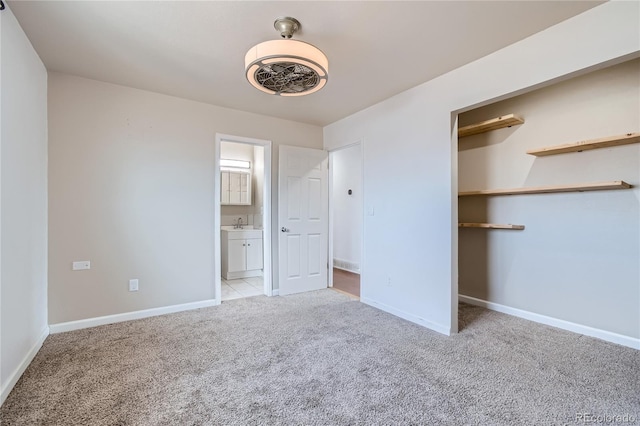 unfurnished bedroom with light carpet, ensuite bath, a spacious closet, and baseboards